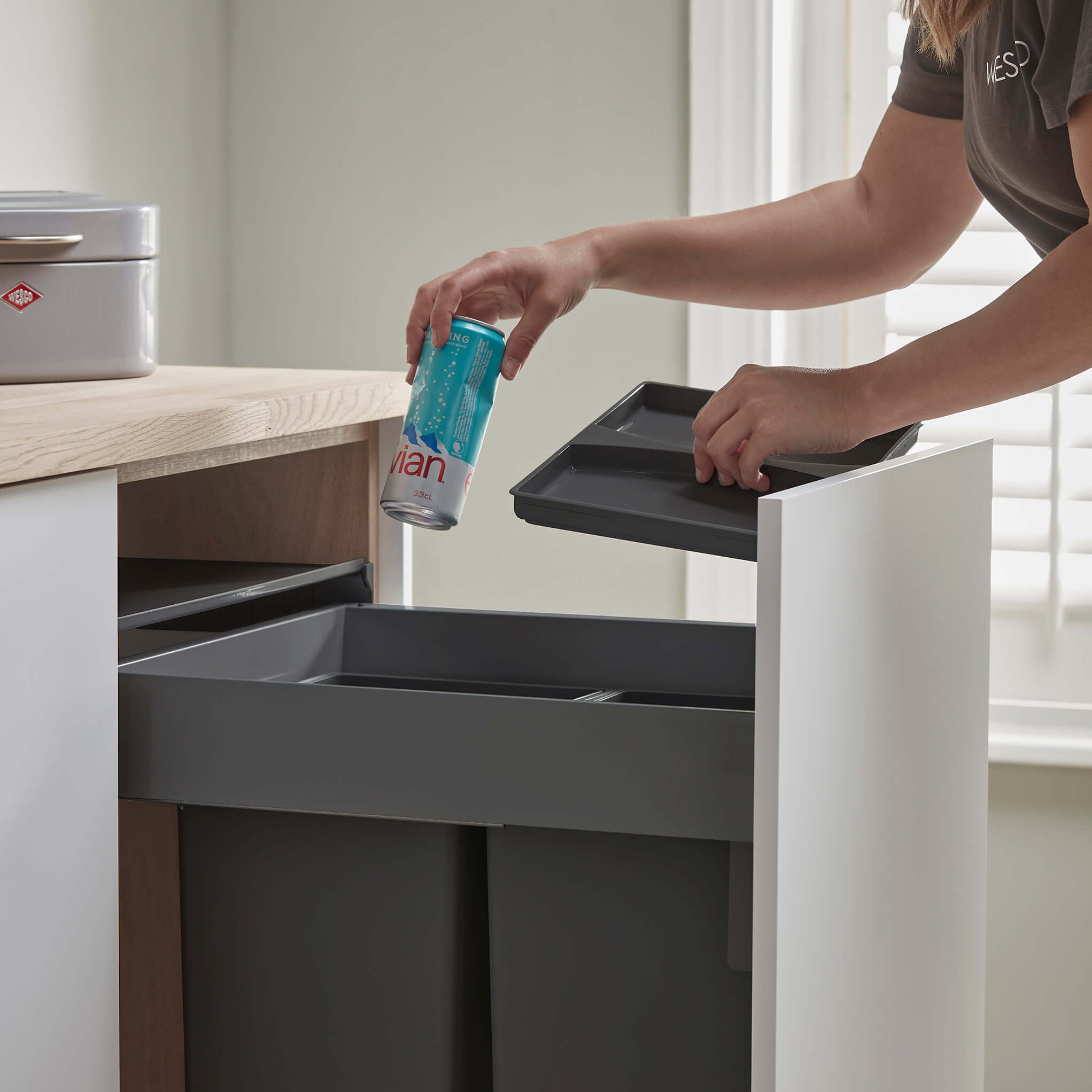 Person placing a can into a Wesco pullboy Z for Merivobox pull-out waste bin.
