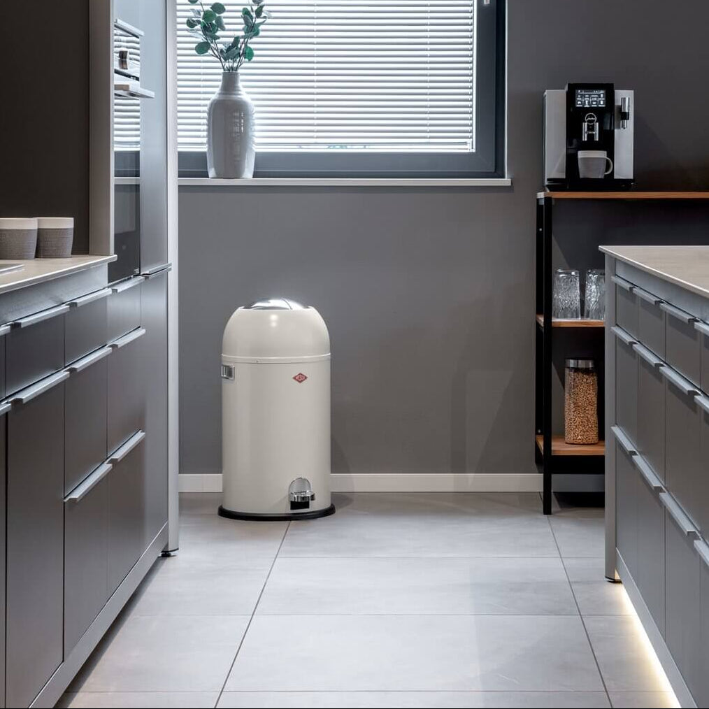 Wesco Kickmaster pedal bin in white with chrome pedal and black base ring in a dark grey kitchen with light tiled flooring
