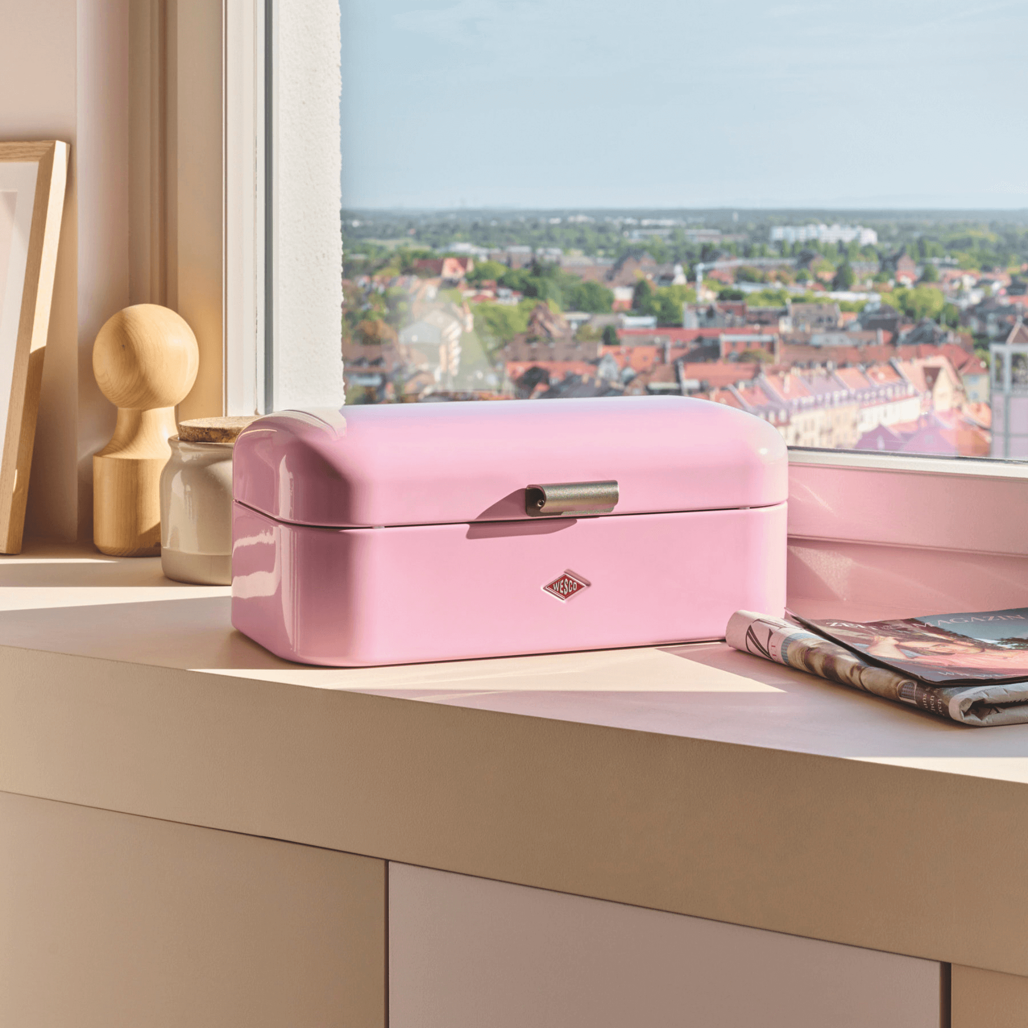 Wesco Pink Grandy on a window ledge with a cityscape view through a window