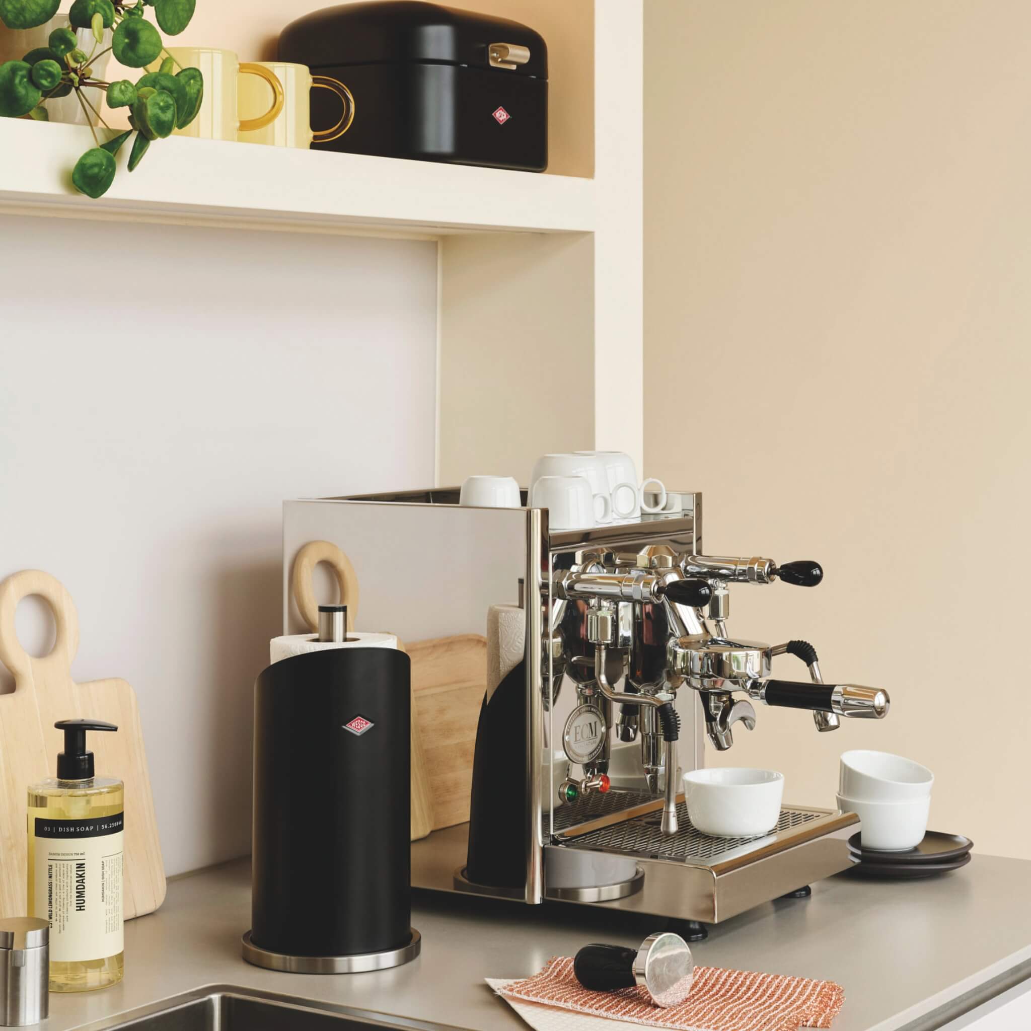 Wesco Matt black circular kitchen roll holder in a modern kitchen lifestyle place next to a barista style coffee machine
