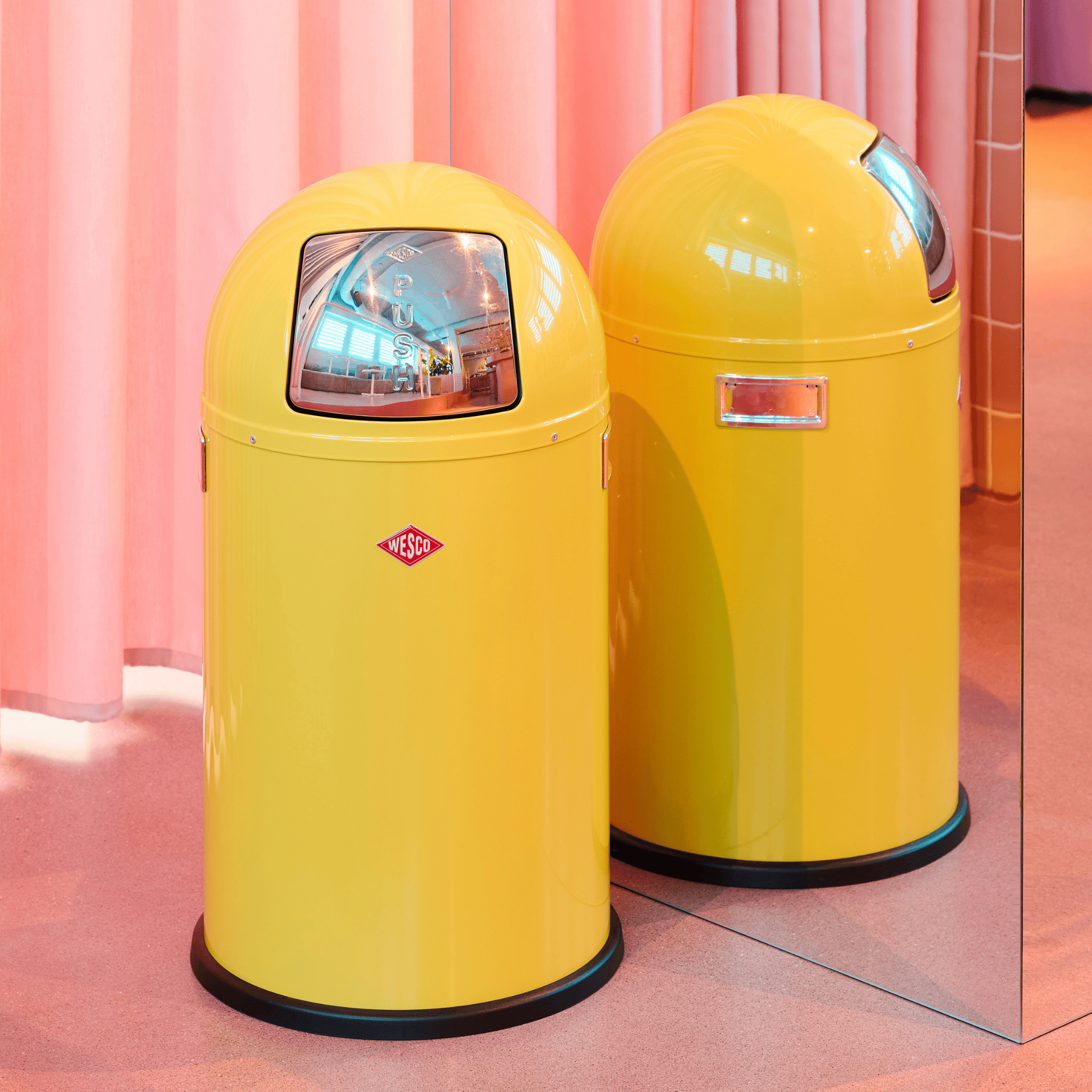 Wesco ushboy Junior 22L Waste Bin in Lemon Yellow with a pink Mirror background