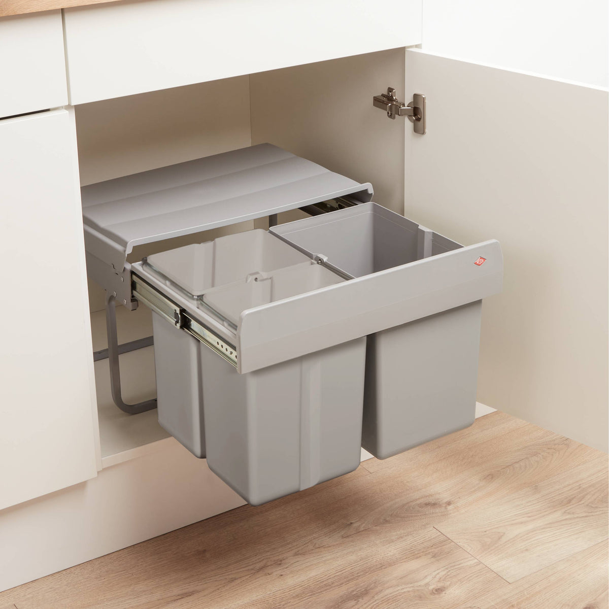 Wesco Shorty Trio under-sink bin with 3 compartments, shown partially extended inside a white kitchen cabinet on a wood floor.