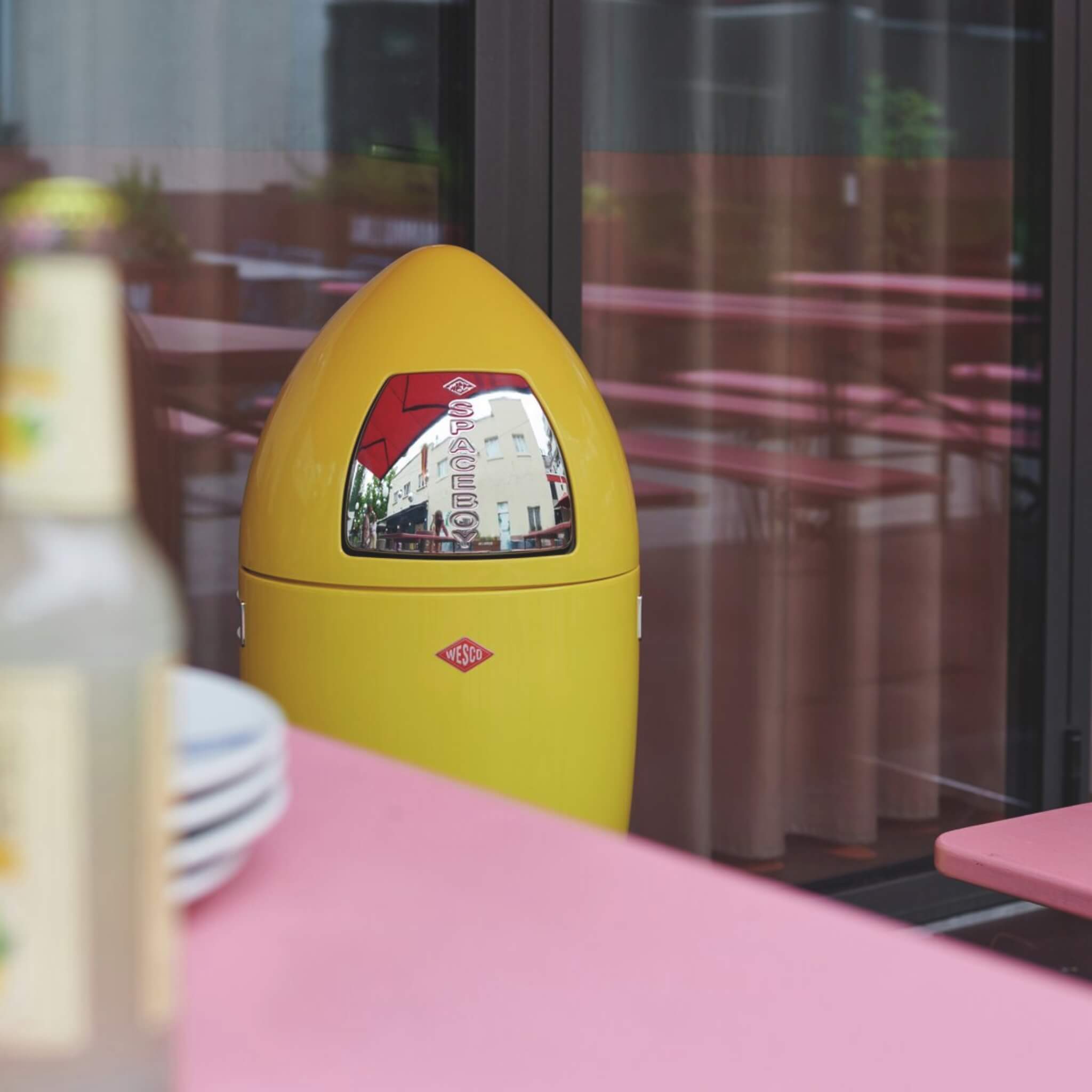 Wesco Lemon Yellow Spaceboy XL Highlighting the top detail of the push flap. Placed outside with bin tables and benches.
