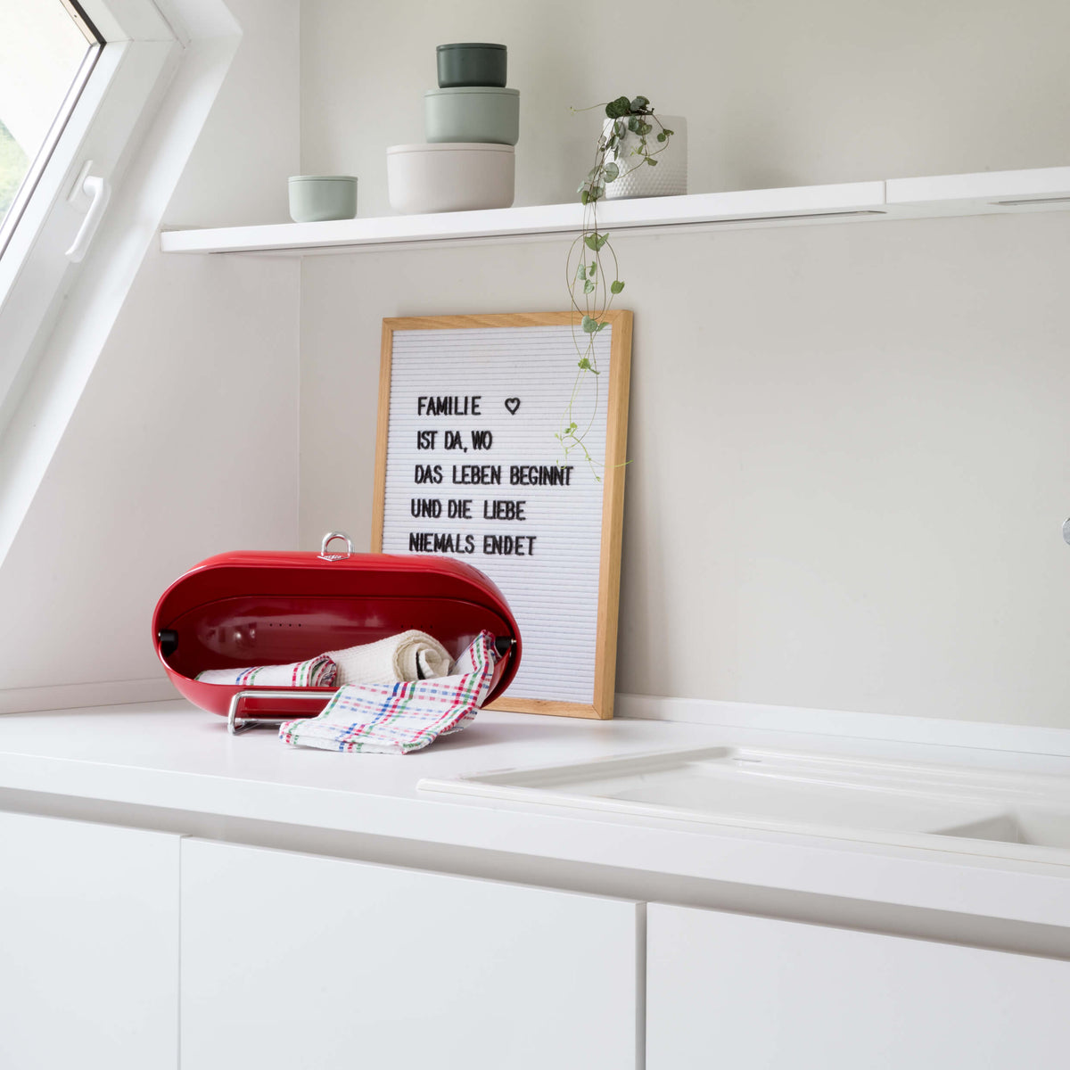 A bright, modern white kitchen or bathroom corner with a white countertop. Including a Wesco Breadboy in red housing tea towels and dish cloths