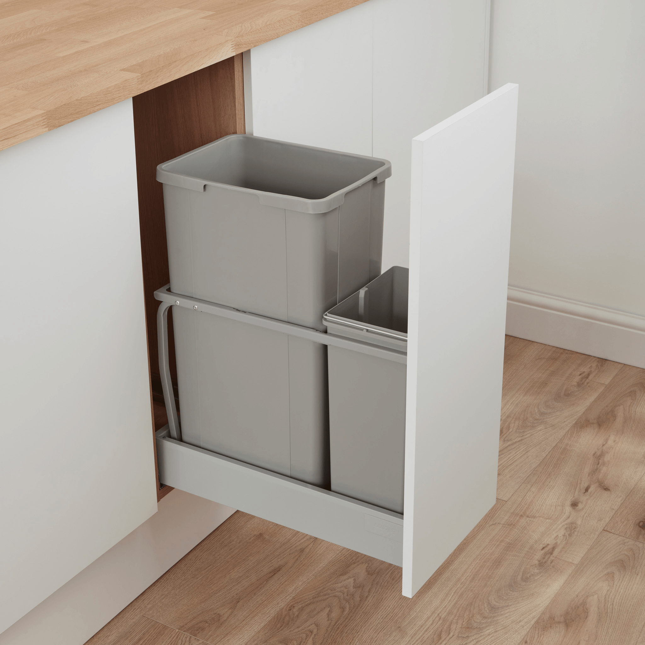 Wesco pull-out under-cabinet waste bin organiser with two grey bins, in a white kitchen cabinet with a wood countertop and light wood floor.