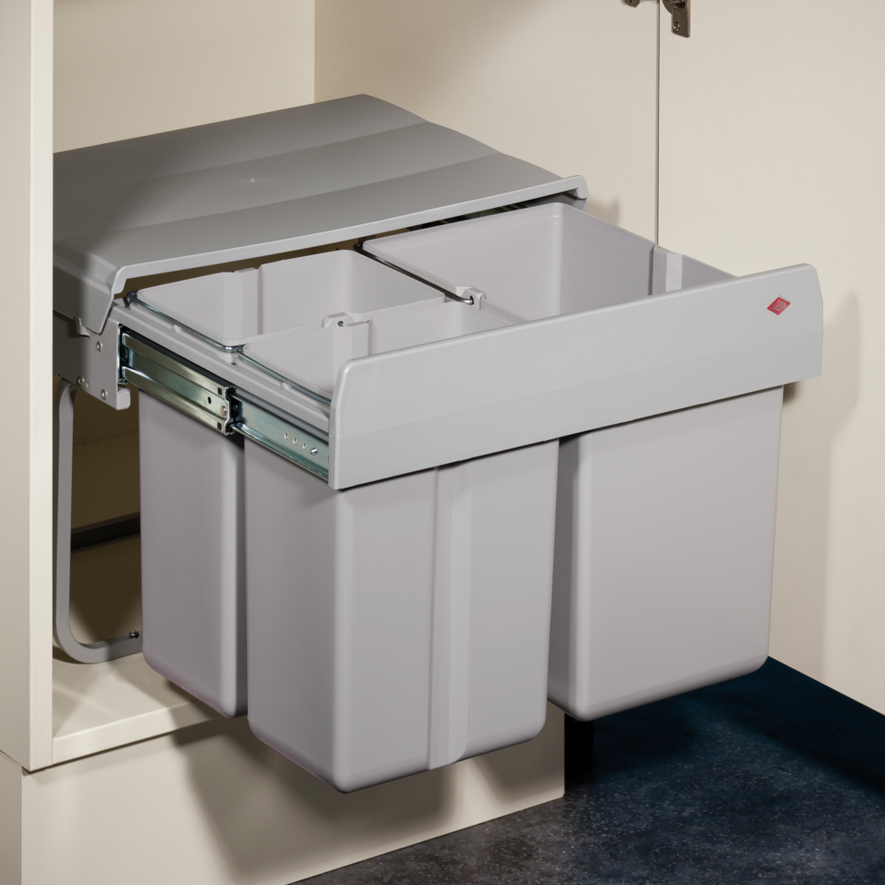 Wesco Shorty Trio A pull-out double bin trash can with three light grey plastic bins and a matching lid, shown installed inside a white under-cabinet space.