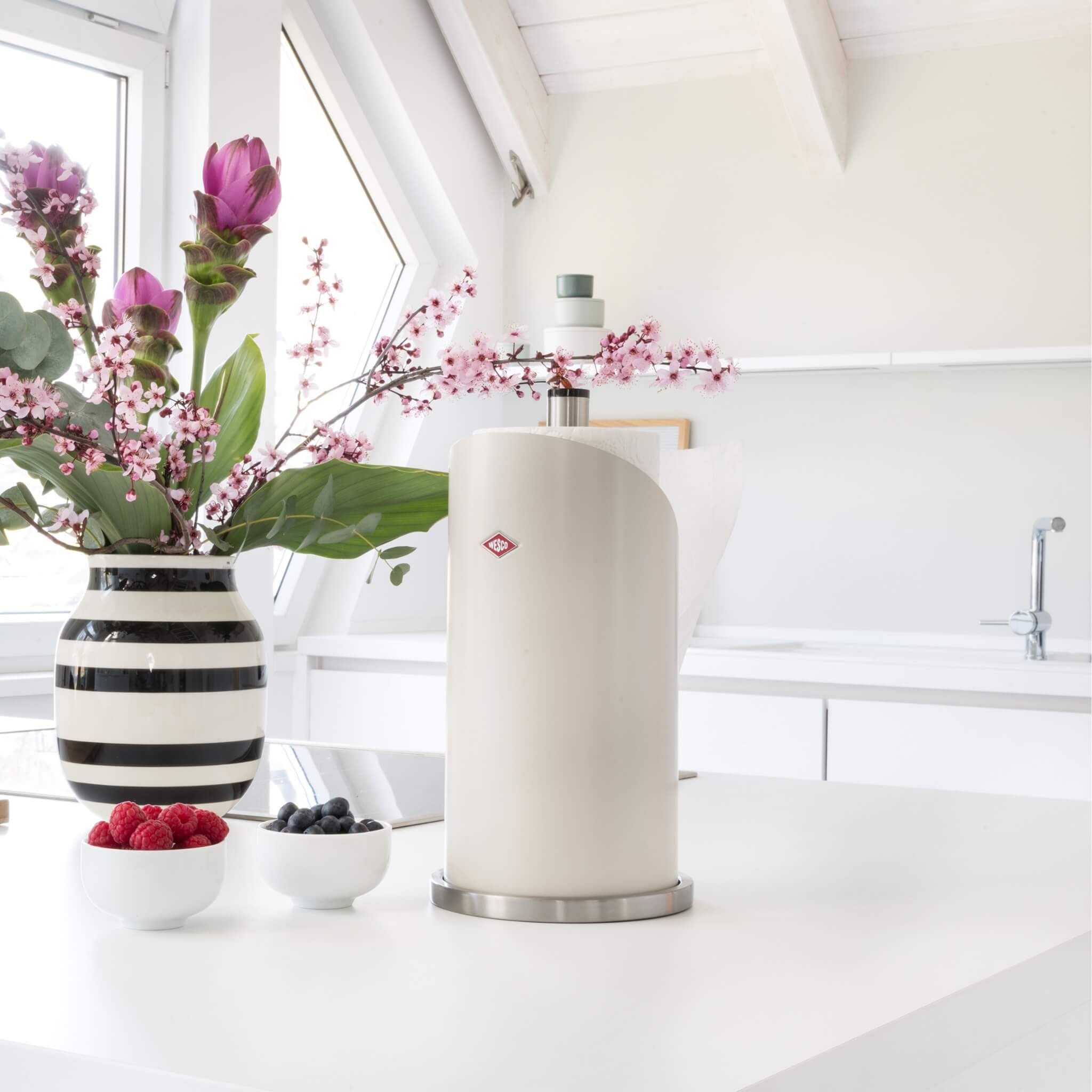Wesco Paper roll holder in matter sand in a crisp white modern kitchen with pink flowers in a black and white strip vase