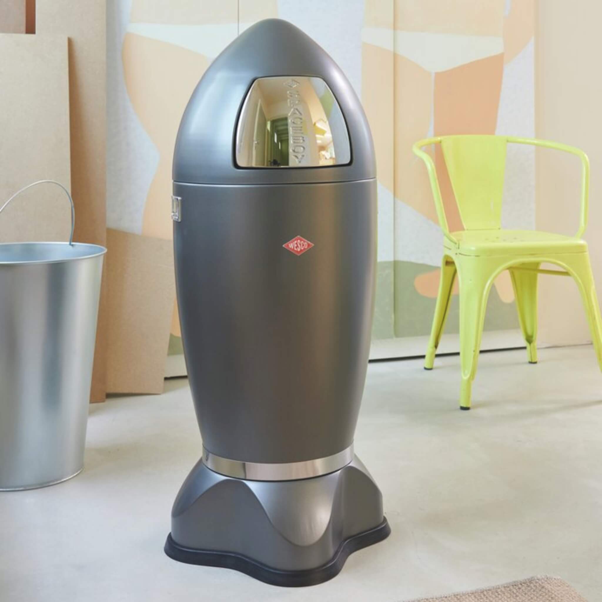 Lifestyle image of the Wesco Paceboy XL in Matt Graphite with a Green chair in the background and peach toned wall colours.