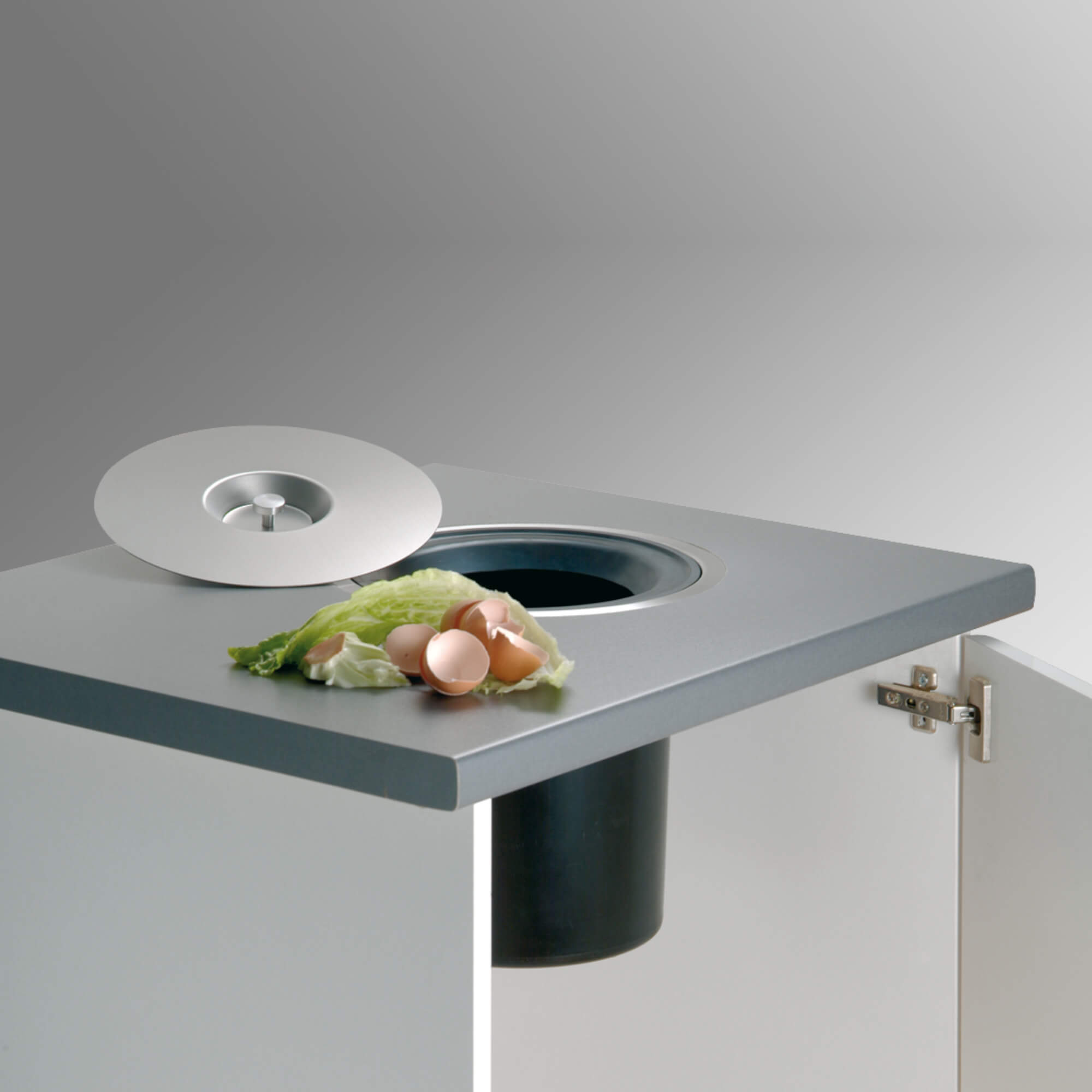 A small stainless steel kitchen bin with a removable bucket, fitted into a counter top, with a silver lid and fixing ring visible.